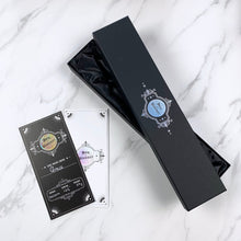 Load image into Gallery viewer,  A sleek black wand box adorned with holographic accents, exuding a luxurious and mysterious vibe. The box is elegantly designed to securely hold a wand, while a shimmering certificate rests beside it, featuring holographic details that catch the light. This exquisite packaging enhances the overall presentation, making it a perfect gift for collectors and fantasy enthusiasts.