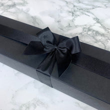 Load image into Gallery viewer, An elegant black wand box adorned with a grand satin black bow, adding a touch of sophistication. The box features a sleek, matte finish that contrasts beautifully with the lustrous bow, making it an eye-catching presentation. Ideal for gifting, the box exudes a sense of luxury and anticipation, perfect for any fantasy enthusiast's prized wand.