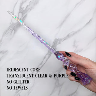 Handmade purple magic wand with  iridescent core. 
Held by a hand with black pointed finger nails on a white marble background. 