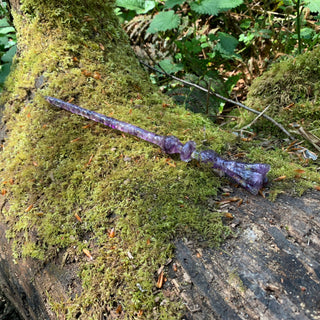 A unique handmade magic wand made with real purple amethyst crystal chips, in the Flora Design. Shown on a mossy log in an enchanting woodland