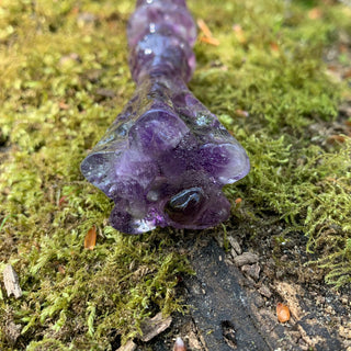 A unique handmade magic wand made with real purple amethyst crystal chips, in the Flora Design. 
The detailed end of the wand is in the shape of a flower and the background is a moss covered log. 