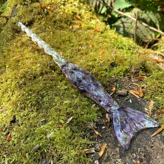 A unique handmade magic wand made with real purple amethyst crystal chips, in the Mertail  Design. 

The background is a moss covered log in a forest. 