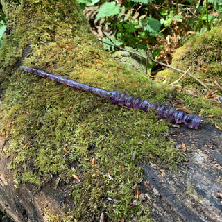 A unique handmade magic wand made with real purple amethyst crystal chips, in the Orbit  Design. 

The background is a moss covered tree in a forest