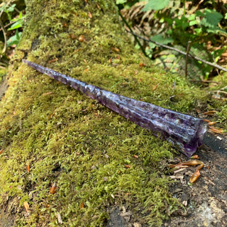 A unique handmade magic wand made with real purple amethyst crystal chips, in the Star  Design. 

The background is a mossy log in a woodland setting.