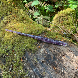 A unique handmade magic wand made with real purple amethyst crystal chips, in the Twist  Design. 

The wand is on a moss covered log in a forest.