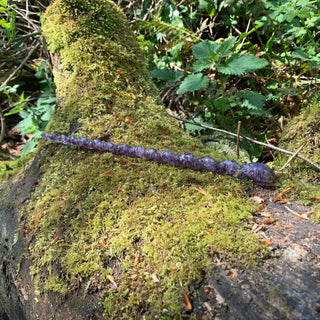 A unique handmade magic wand made with real purple amethyst crystal chips, in the Unicorn  Design. 

On a moss covered log in a forest. 
