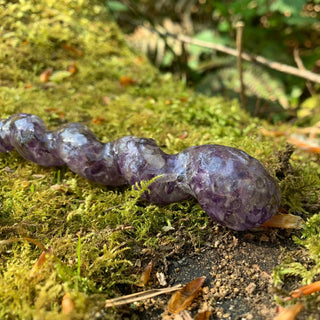 A unique handmade magic wand made with real purple amethyst crystal chips, in the Unicorn  Design. 

The spiral base of the wand is on a mossy log in a woodland. 