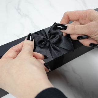 luxury wand box being adorned with a black satin bow by a witch with black pointed nails