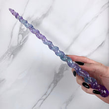 Load image into Gallery viewer, A stunning blue and purple unicorn magic wand featuring a delicate, translucent design with iridescent shimmering accents and glitter. The wand has a gracefully tapered shaft that sparkles in light, showcasing its intricate craftsmanship. Perfect for fantasy collectors, this wand embodies elegance and enchantment, making it a prized addition to any magical assortment.
