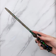 Load image into Gallery viewer, A stunning black Flora magic wand featuring a delicate, translucent design with iridescent shimmering accents. The wand has a beautiful flower shaped base with a narrow shaft that sparkles in light, showcasing its intricate craftsmanship. Perfect for fantasy collectors, this wand embodies elegance and enchantment, making it a prized addition to any magical assortment.
