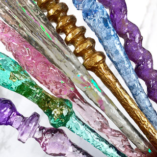 close up of mystery wands in the colours purple , green , pink, grey, gold, and blue.  The various designs show some with glitter and some with an iridescent wand core