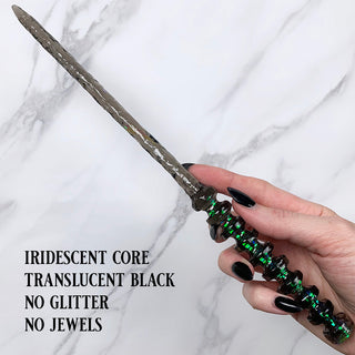 Handmade black magic wand with  iridescent core. 
Held by a hand with black pointed finger nails on a white marble background. 