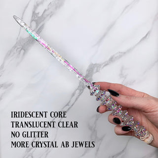 Handmade clear magic wand with  iridescent core and AB jewels. 
Held by a hand with black pointed finger nails on a white marble background. 