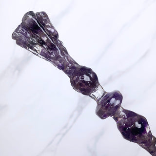 A unique handmade magic wand made with real purple amethyst crystal chips, in the Flora Design. 
Showing the detail of the base of the wand on a white marbled background.