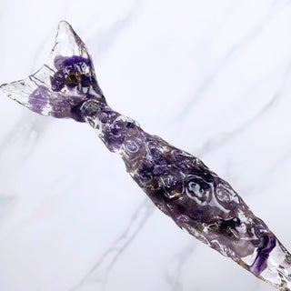 TA unique handmade magic wand made with real purple amethyst crystal chips, in the Mertail  Design. 

Showing the detail of the mermaid shaped base of the wand on  a white marbled background.
