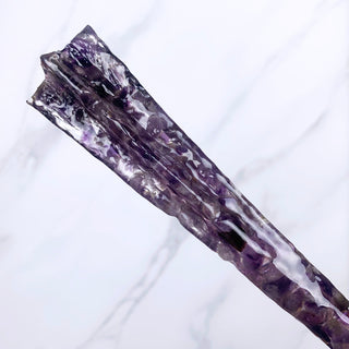 A unique handmade magic wand made with real purple amethyst crystal chips, in the Star  Design. 

The detail of the handle of the wand is on a white marbled background.