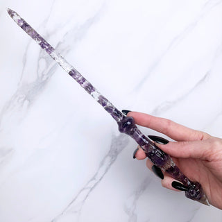 A unique handmade magic wand made with real purple amethyst crystal chips, in the Stiletto  Design. 

On a white marbled background being held by a hand with black pointed nails. 