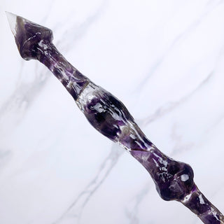 A unique handmade magic wand made with real purple amethyst crystal chips, in the Stiletto  Design. 

The close up detail of the pointed base of the wand is on a white marbled background.