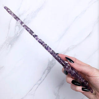 A unique handmade magic wand made with real purple amethyst crystal chips, in the Twist  Design. 

On a white marbled background being held by a hand with black pointed nails. 