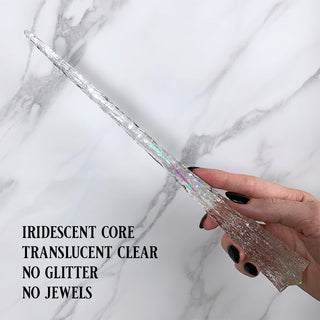 Handmade clear magic wand with  iridescent core.
 
Held by a hand with black pointed finger nails on a white marble background. 