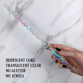 Handmade clear magic wand with  an iridescent core. 
Held by a hand with black pointed finger nails on a white marble background. 