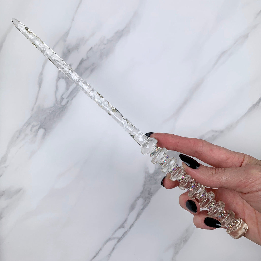 A stunning clear celestial-inspired Orbit design magic wand featuring a delicate, translucent design with iridescent shimmering accents. The wand has a beautiful handle with alternating hoops with a narrow shaft that sparkles in light, showcasing its intricate craftsmanship. Perfect for fantasy collectors, this wand embodies elegance and enchantment, making it a prized addition to any magical assortment.