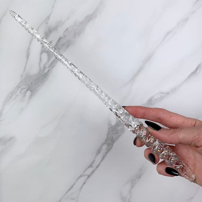 A stunning clear Twist design magic wand featuring a delicate, translucent design with iridescent shimmering accents. The wand has a beautiful twisted handle with with a narrow shaft that sparkles in light, showcasing its intricate craftsmanship. Perfect for fantasy collectors, this wand embodies elegance and enchantment, making it a prized addition to any magical assortment.
