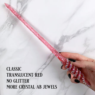 Handmade red  magic wand with  AB jewels. 
Held by a hand with black pointed finger nails on a white marble background. 