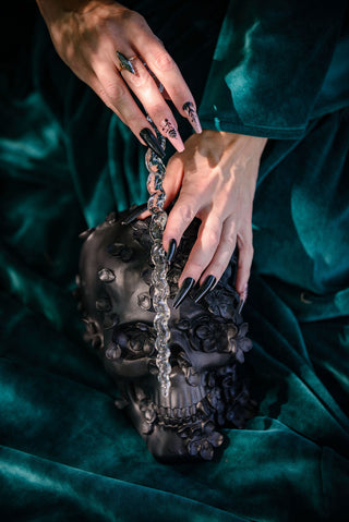 Witch in a green dress holding a clear unicorn shaped wand with black skull in background