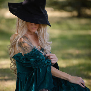 Witch sat on the grass in a green dress and black hat holding a clear unicorn shaped wand