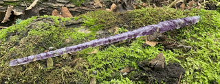 A unique handmade magic wand made with real purple amethyst crystal chips, in the twist Design. 
The background is a moss covered log in a whimsical forest. 