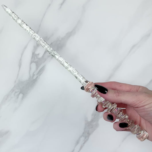 A stunning clear celestial-inspired Orbit design magic wand featuring a delicate, translucent design with iridescent shimmering accents. The wand has a beautiful handle with alternating hoops with a narrow shaft that sparkles in light, showcasing its intricate craftsmanship. Perfect for fantasy collectors, this wand embodies elegance and enchantment, making it a prized addition to any magical assortment.