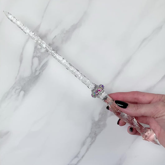 A stunning clear Stiletto design magic wand featuring a delicate, translucent design with iridescent shimmering accents. The wand has a beautiful smooth handle that tapers to a point with a narrow shaft that sparkles in light, showcasing its intricate craftsmanship. Perfect for fantasy collectors, this wand embodies elegance and enchantment, making it a prized addition to any magical assortment.