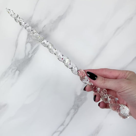 A stunning clear unicorn magic wand featuring a delicate, translucent design with iridescent shimmering accents. The wand has a gracefully tapered shaft that sparkles in light, showcasing its intricate craftsmanship. Perfect for fantasy collectors, this wand embodies elegance and enchantment, making it a prized addition to any magical assortment.